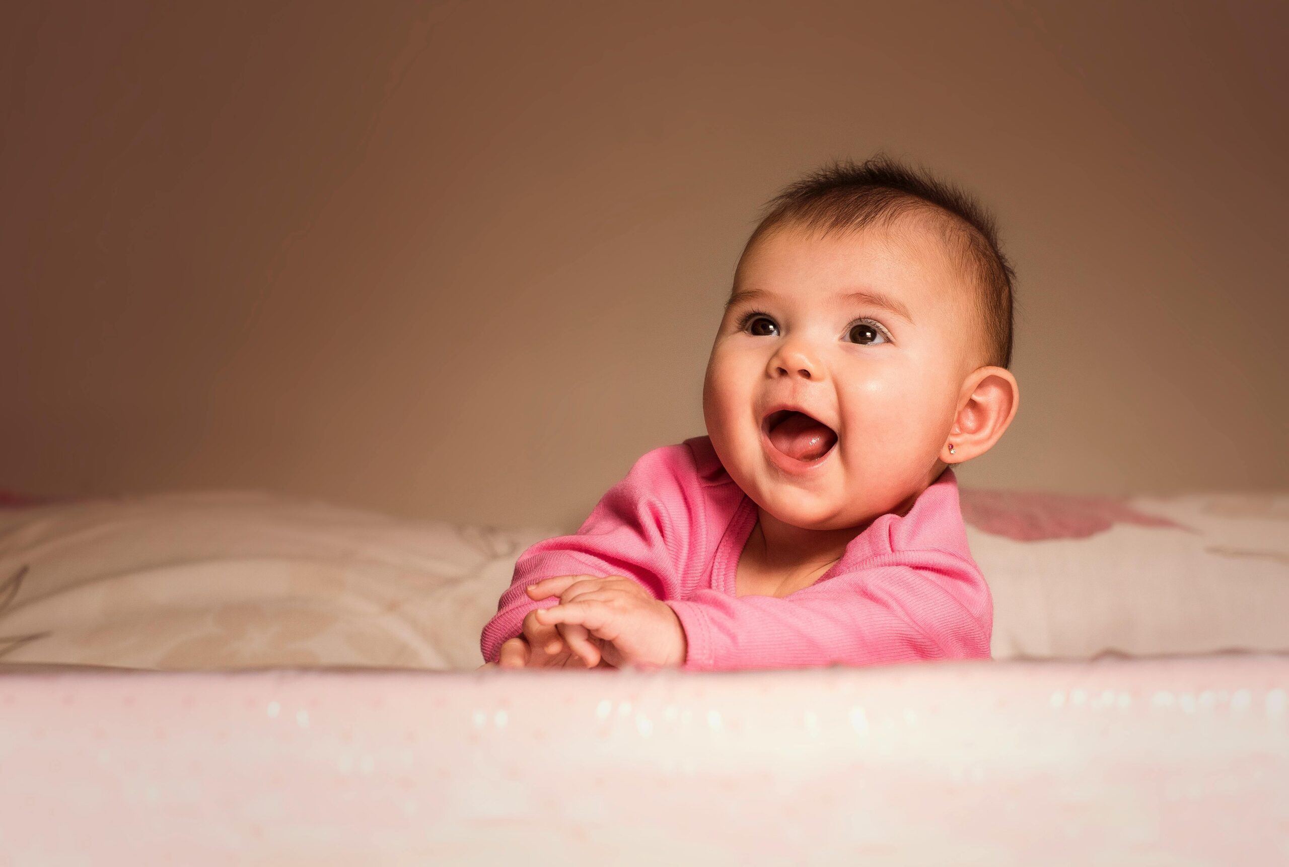 Charming portrait of a smiling baby girl in pink indoors, exuding happiness and innocence.