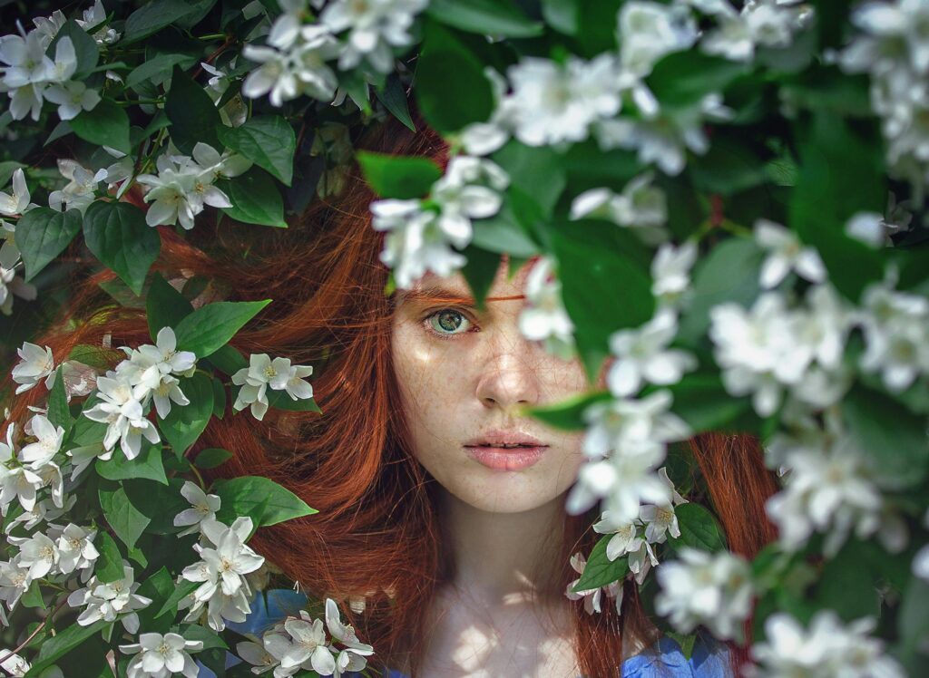 Artistic portrait of a red-haired woman surrounded by white flowers.