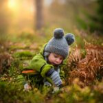 A cute baby in a knit hat and green outfit exploring nature during sunset.