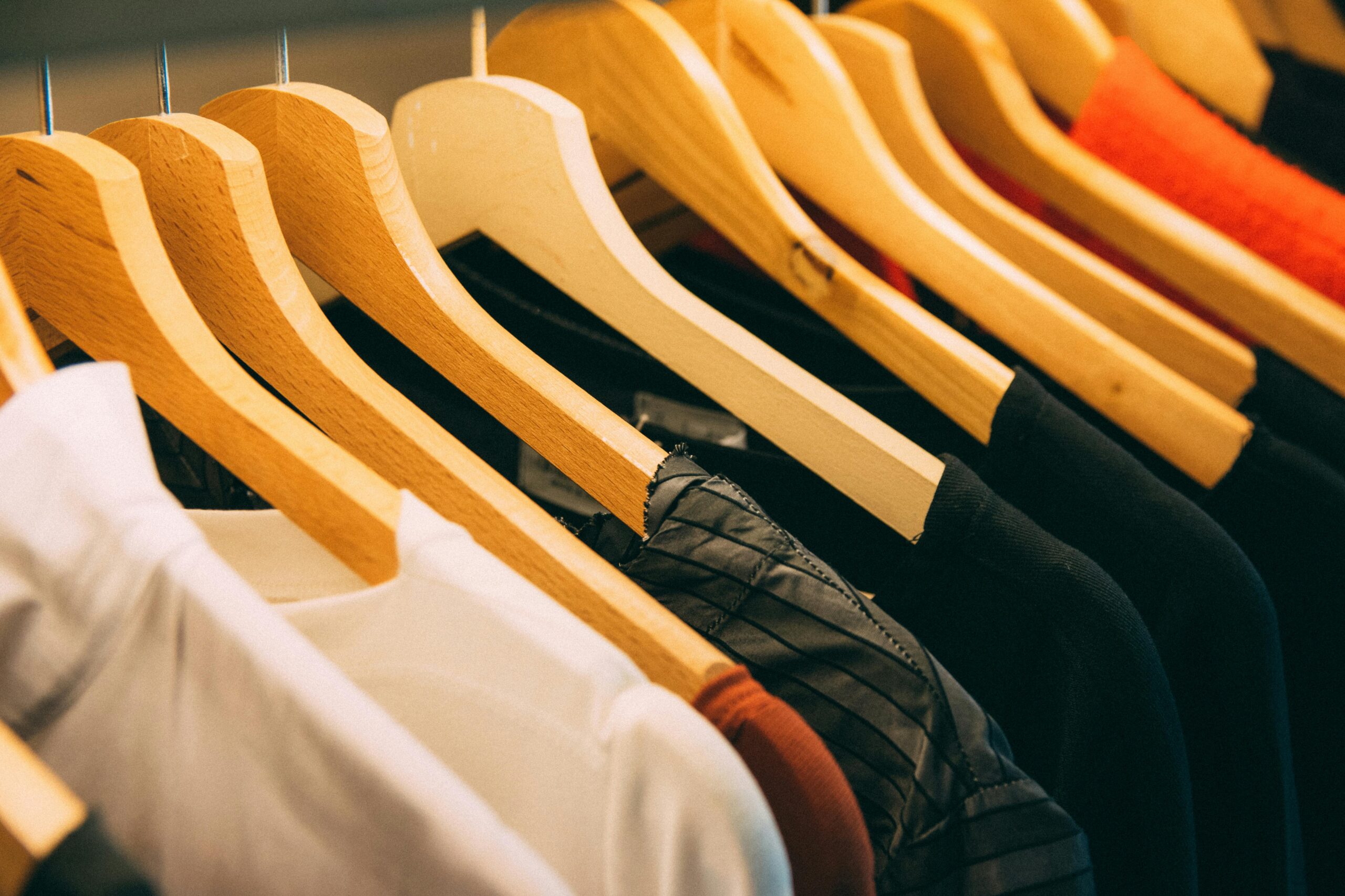 A close-up view of a row of clothes on wooden hangers, showcasing various fabrics and colors in a wardrobe setting.